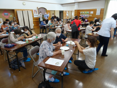 写真：20人ぐらいのご年配の方々が、長机の上で芳香剤を作っている様子