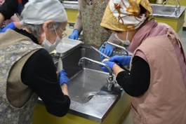 写真：ご年配の女性２人が、水道の蛇口の前で作業をしている様子